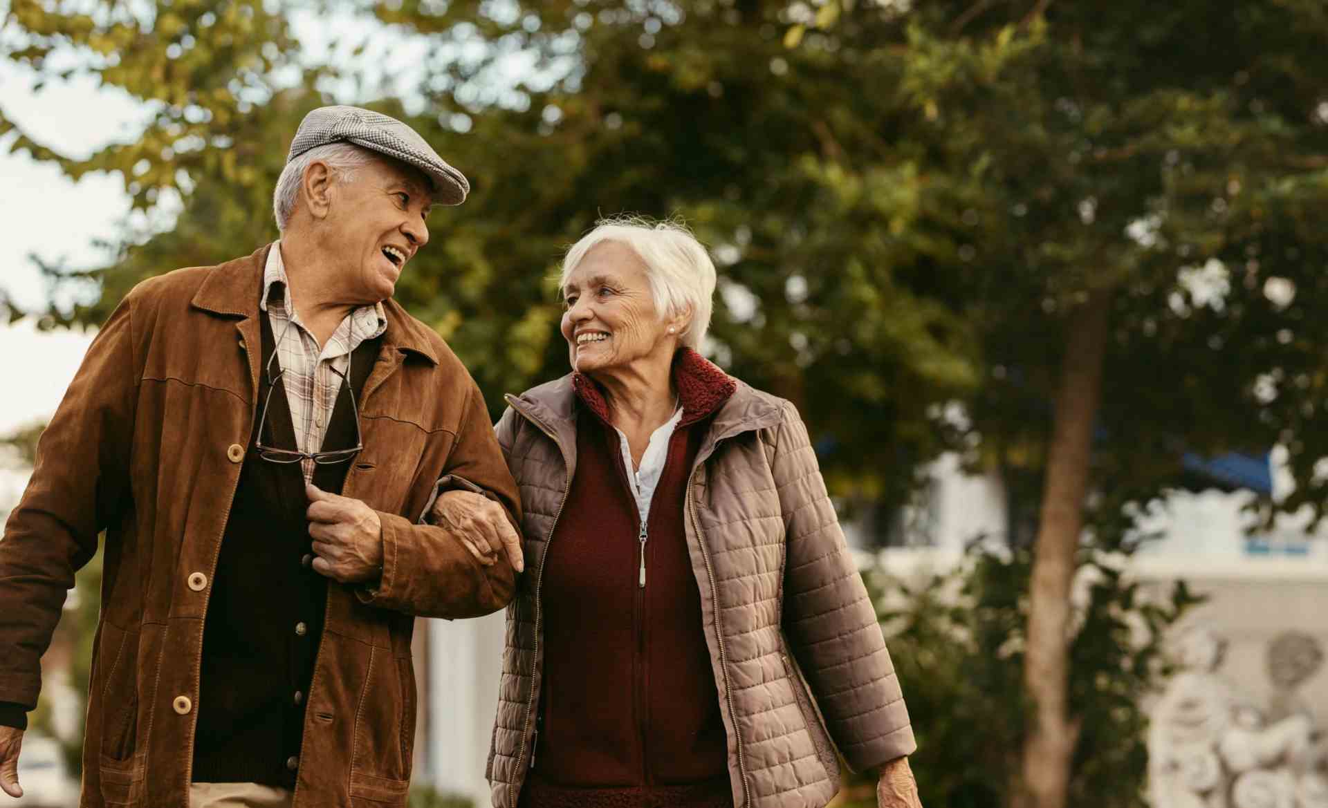 An elderly couple linking arms walking in a park